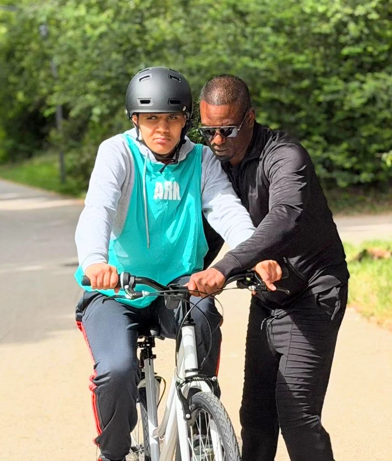 Jeune à vélo guidé par un intervenant sur une piste arborée